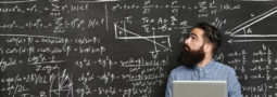 person at laptop in front of chalkboard covered in different formulas