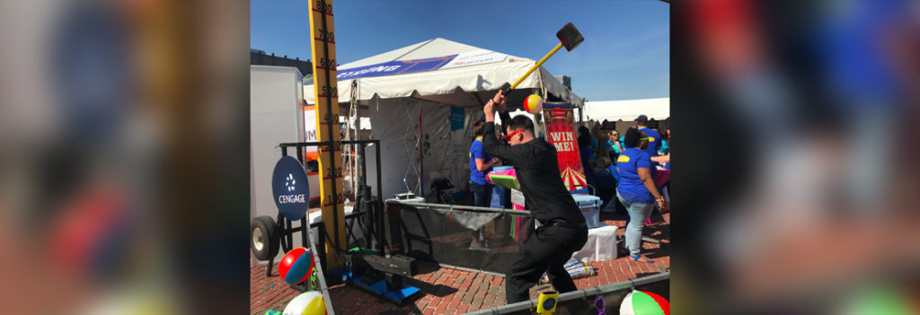 Man lifting oversized hammer overhead at Cengage's strength measure booth