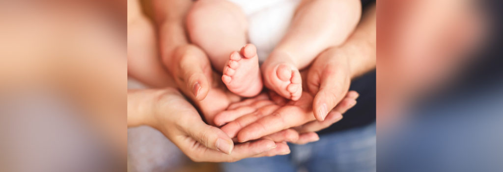 two sets of adult hands holding baby's feet