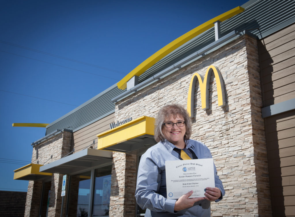 Graduate holding certificate in front of McDonald's