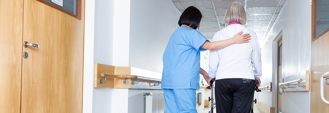 picture of healthcare wroking helping someone walk down hospital hallway
