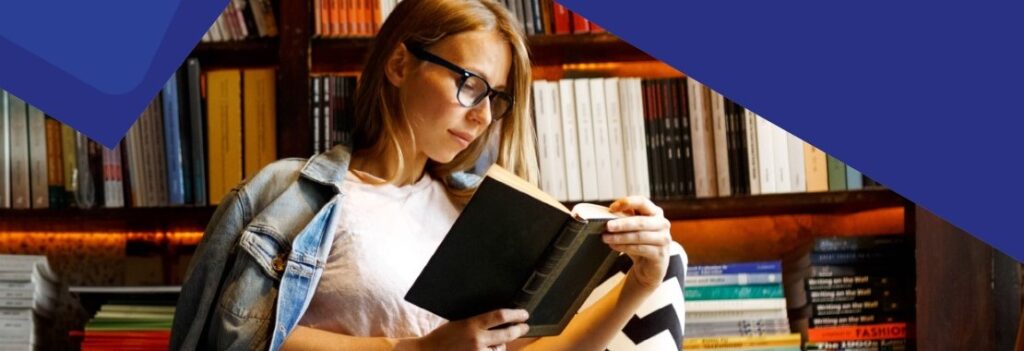 Woman with eyeglasses in front of bookshelves sits reading a book