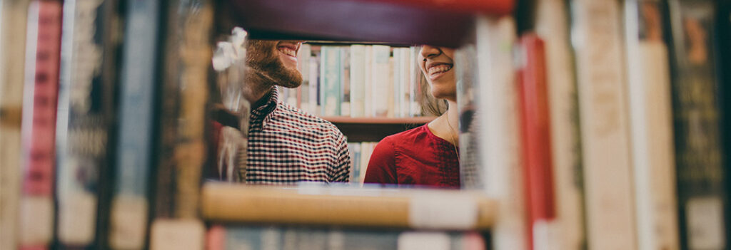 A view of two teachers from an opening in a bookcase