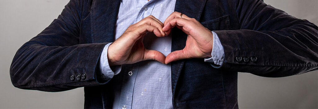 Person wearing a blazer and buttoned short shapes hands into a heart.