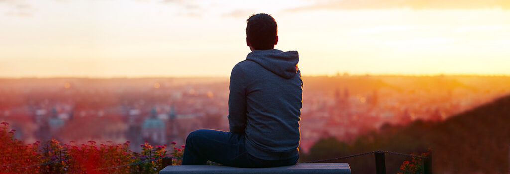 A student looking over a city skyline at sunset