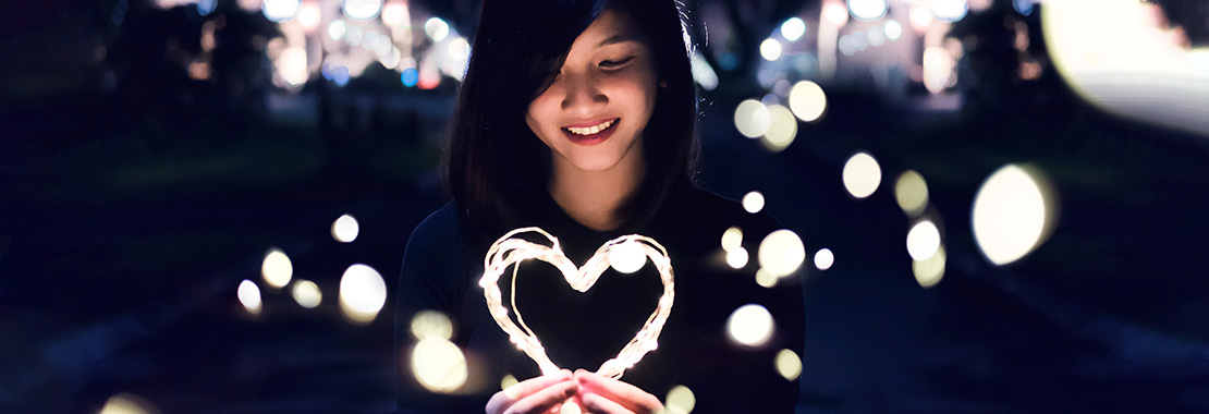 A smiling young woman holds an illuminated heart