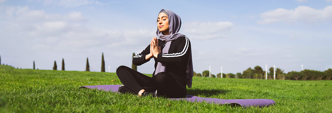 Photo of a woman meditating in a field with her eyes closed and hands pressed together.