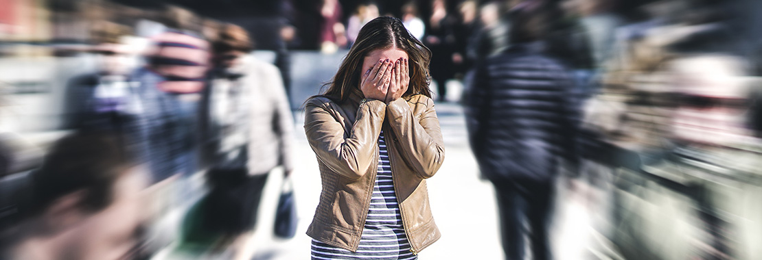 A female student covers her face with her hands with a blurred background of people walking