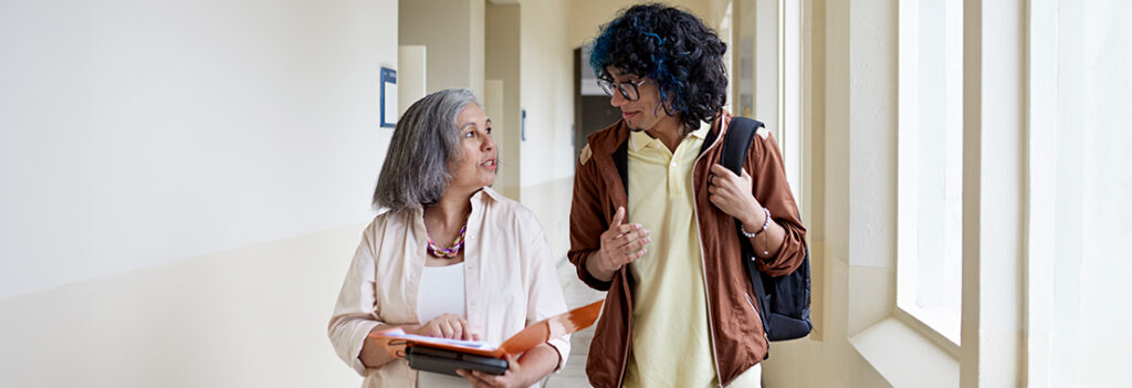 A teacher and student converse in the hallway