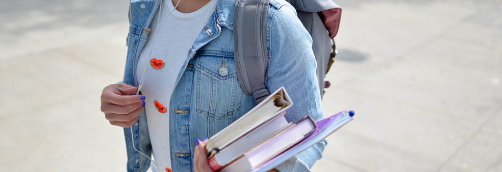 A student walking with binders in hand.