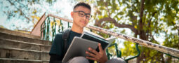 Image of a student reading a Psychology textbook while sitting on a set of stairs outdoors.