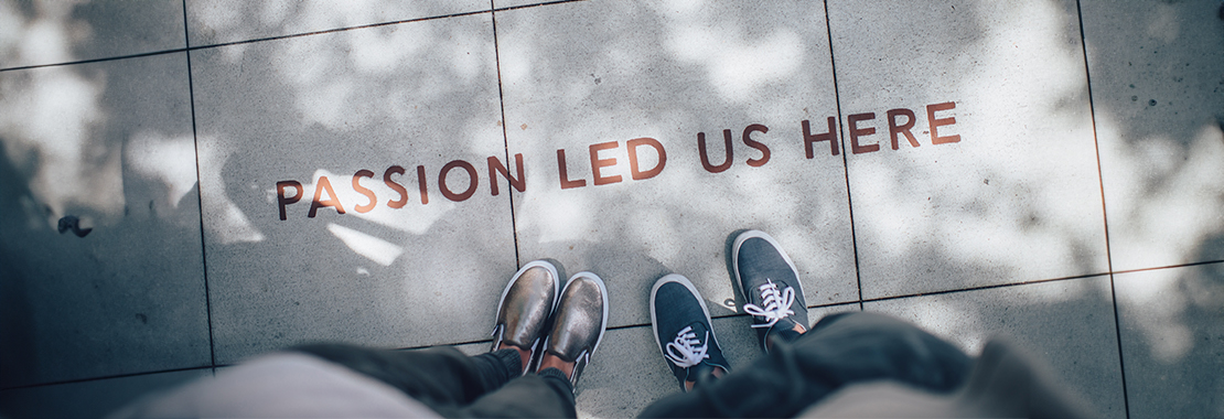 Photograph of two people's feet on the ground, with the words "Passion led us here," written on the ground.