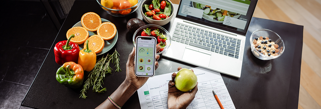 Someone analyzing their diet on their digital devices surrounded by fruits and vegetables