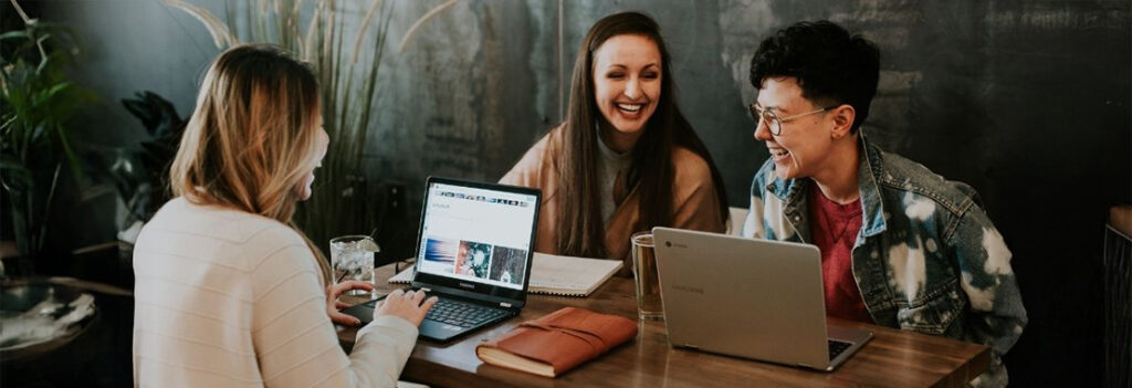 Three students chat while working on laptops