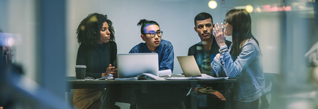 Four individuals sitting at a table with laptops.