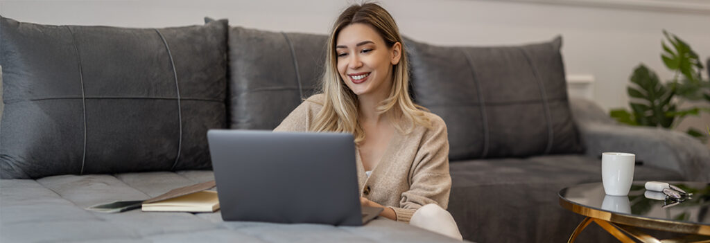 A woman uses her laptop while sitting on the floor near her couch.