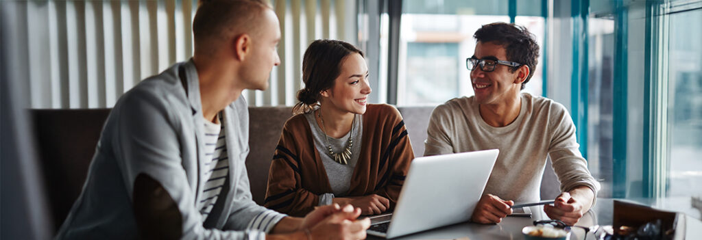 Three people are seated at a table with a laptop in front of them.