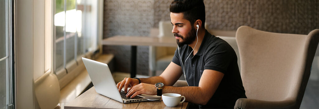 An individual with earbuds in types on their laptop.