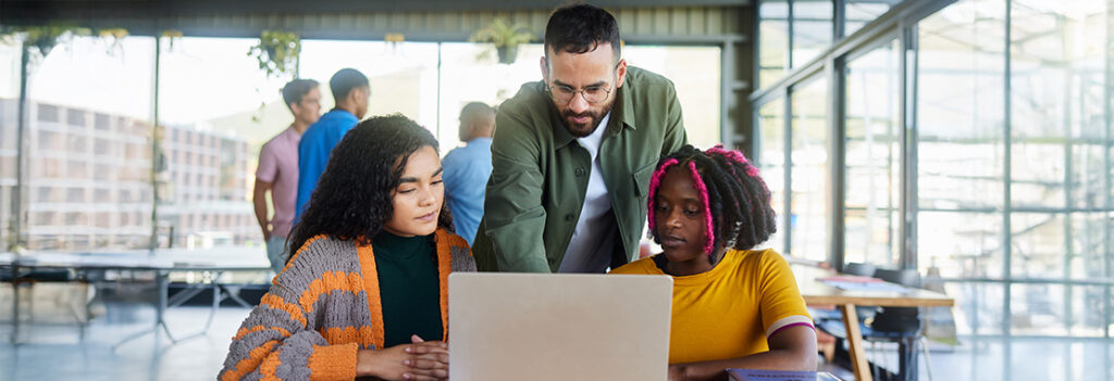 Three individuals surround an open laptop.