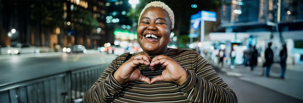 A smiling person makes a heart shape with their hands.