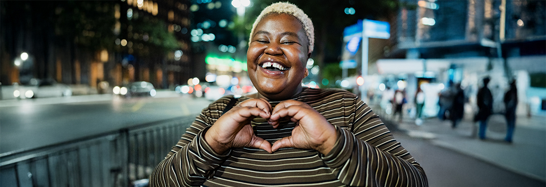 A smiling person makes a heart shape with their hands.